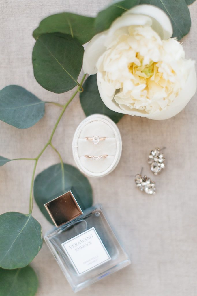 Wedding rings, jewelry, and perfume styled with peonies