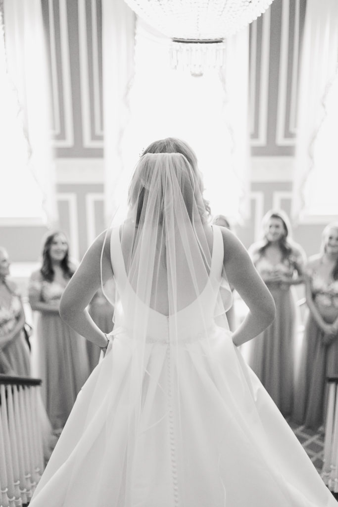 Black and white image of a bride coming down the stairs to greet her bridesmaids at a Genesee Valley Club wedding