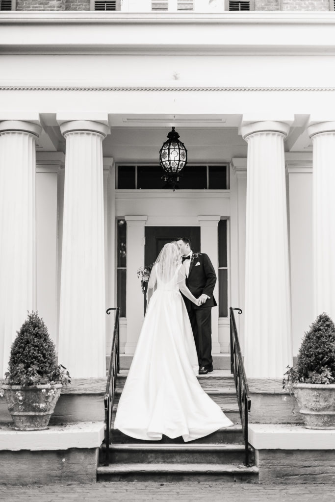Black and white image of a wedding couple kissing on the venue's front steps