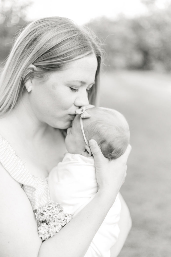 A black and white image of a mother gently kissing her newborn daughter on the forehead.