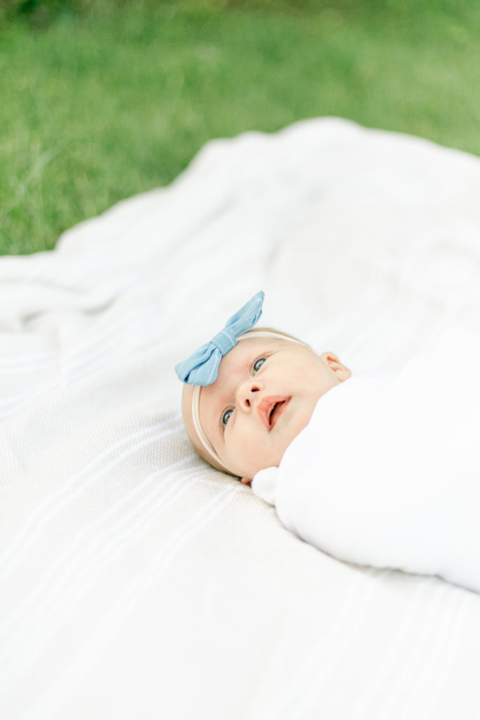 A newborn photoshoot with a baby laying on a blanket in the grass.