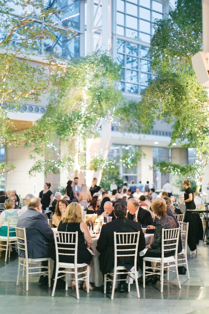 A reception full of guests and lit by twinkle lights, at a Wintergarden wedding in downtown Rochester, NY.