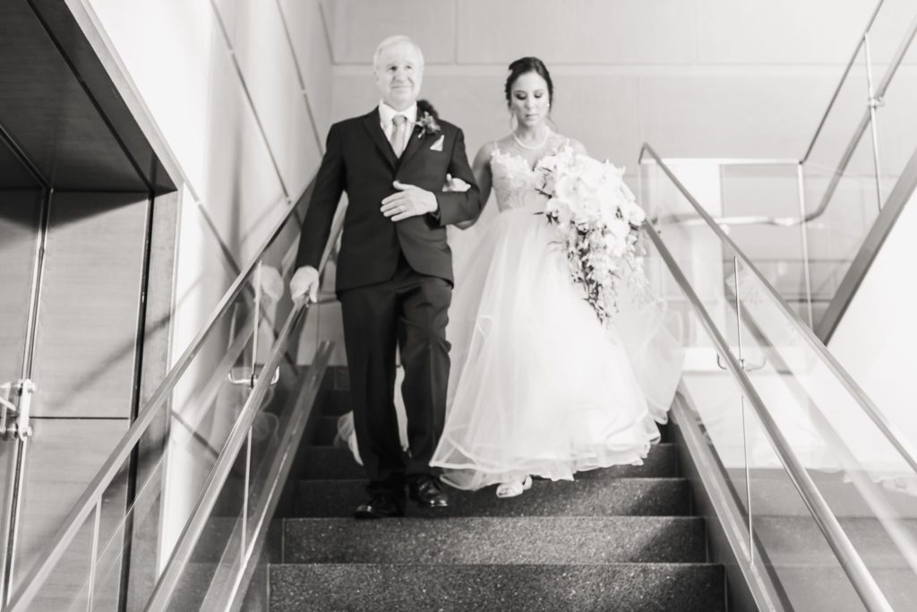 Black and white image of a bride and her father walking down the staircase at a Wintergarden wedding.