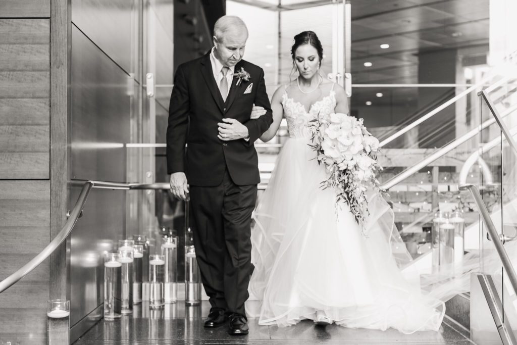 Black and white image of a bride and her father walking down the aisle at a Wintergarden wedding in Rochester, NY.