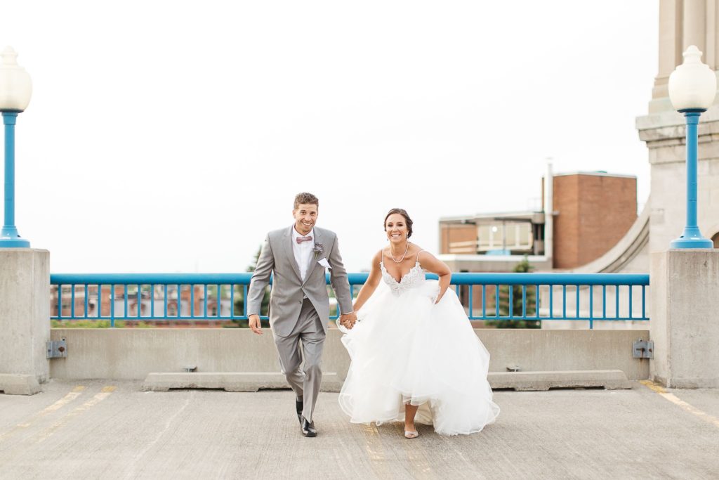 A bride and groom running across a downtown Rochester, NY rooftop.