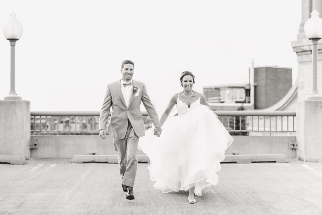Black and white image of a bride and groom running across a downtown Rochester, NY rooftop.