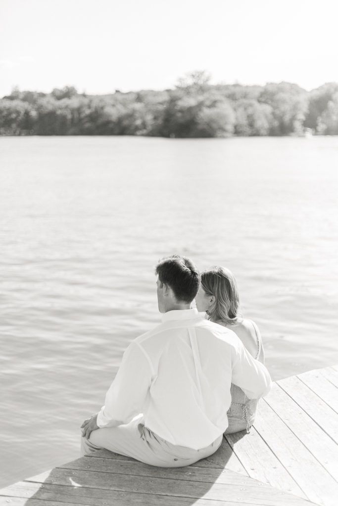An engaged couple sitting on the dock at The Lake House on Canandaigua during an engagement portrait session. 