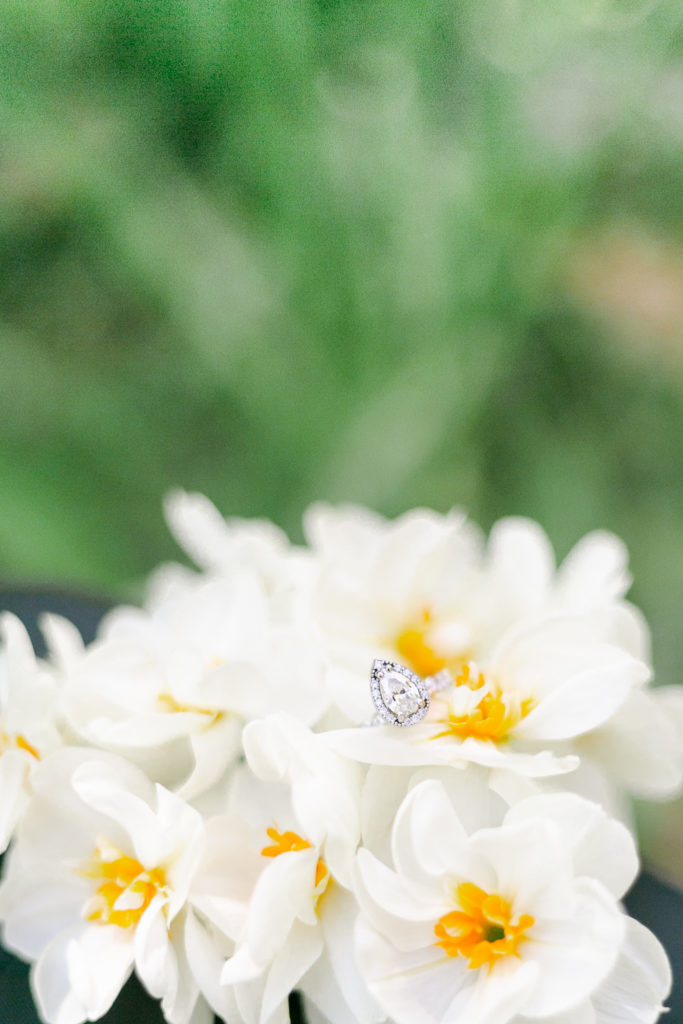 An engagement ring nestled among a bunch of yellow daffodils.