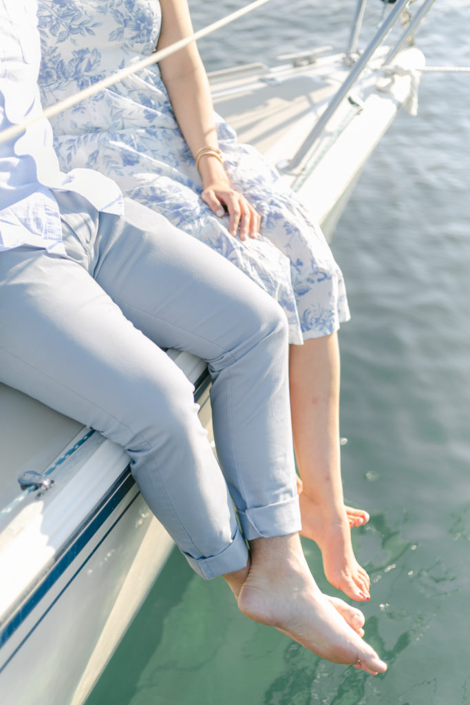 A couple holding hands and dangling their feet over the edge of a sailboat.