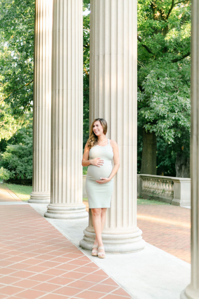 A pregnant woman leans against a column at a Rochester NY maternity photography session.